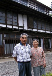 典型的な養蚕農家「三階屋」の前に立つ小林さん夫妻