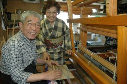 妻、京子さん（右）のため、手機で着物を織る弘一さん（左）