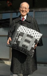 新井淳一さんデザインの布地を生かしたマントをまとい、クッションを手にする島崎さん