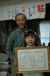 「蚕を通じて子供時代のことを思い出す」と話す山田さんと、入賞した「繭クラフト作品展」の賞状を手にする孫の要ちゃん 