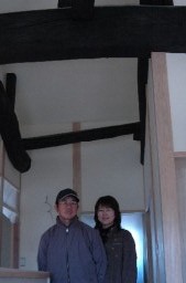 黒光りする梁の下に立つ竹内さんと妻の里美さん