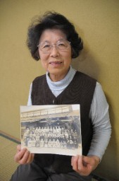 幼い時に宏文館製糸場の前で撮影した写真を手に思いを語る松田さん
